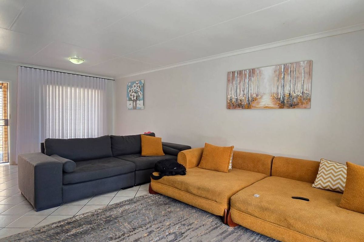 A spacious living room featuring tiled flooring, neutral walls, and a security gate leading to an outdoor area.