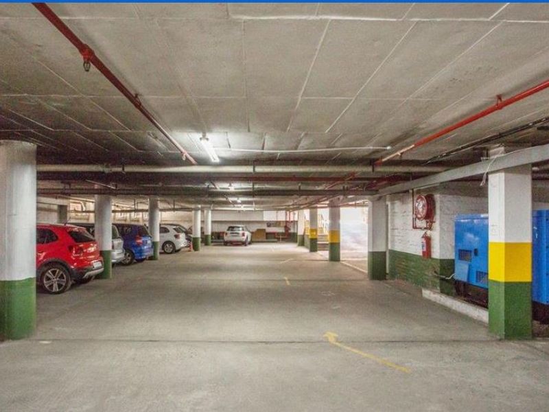 Underground parking garage featuring concrete flooring, structural columns, and integrated fire safety equipment including sprinklers and hose reels.