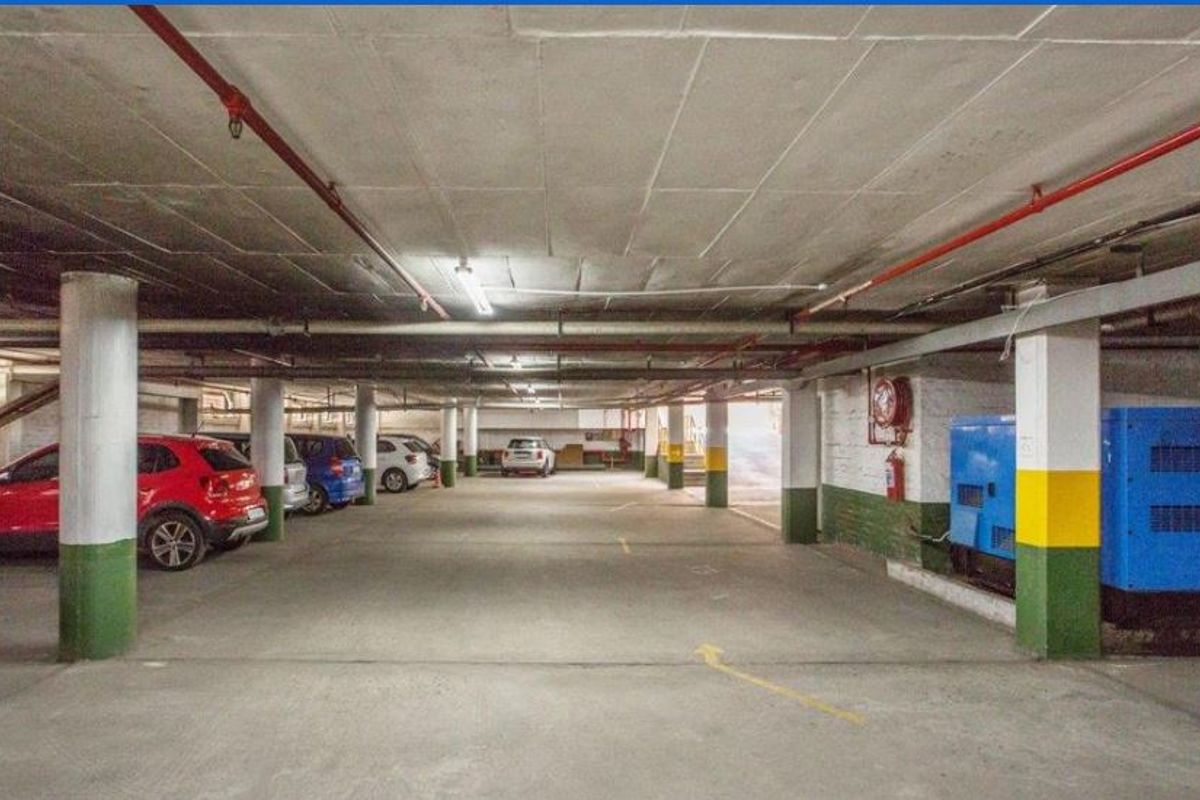 Underground parking garage featuring concrete flooring, structural columns, and integrated fire safety equipment including sprinklers and hose reels.