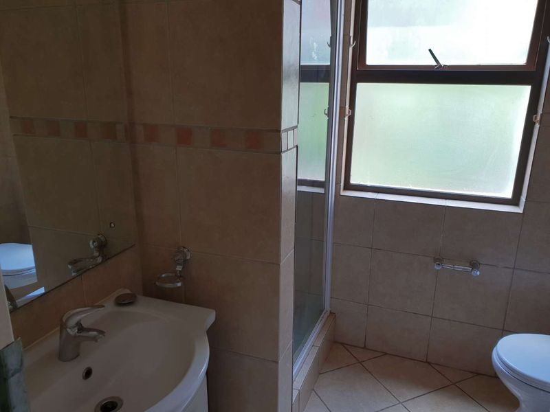 A functional bathroom featuring a pedestal basin, shower enclosure, and toilet with neutral tiled finishes and natural light from a frosted window.