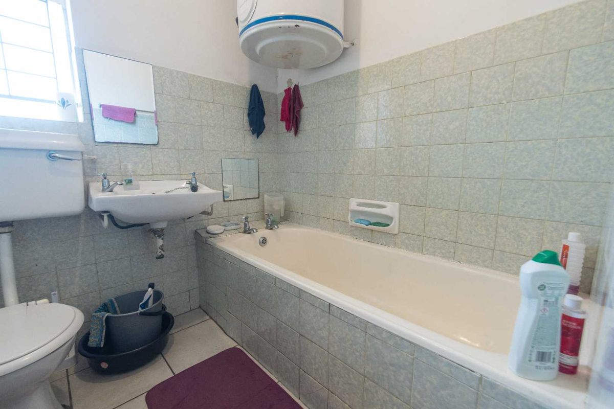 A functional bathroom featuring a standard bathtub, wall-mounted basin, toilet, and an exposed electric water heater unit.