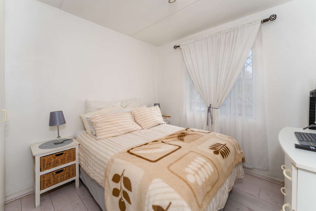 A compact bedroom featuring light-toned laminate flooring and a window with curtain rod installation.