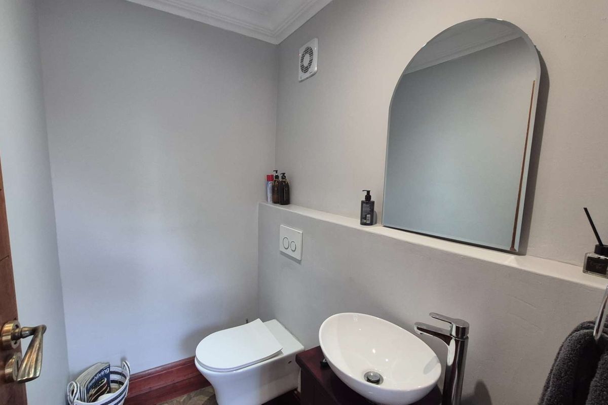 A modern guest bathroom featuring a wall-mounted toilet, a stylish vessel sink with chrome faucet, and an arched wall mirror.