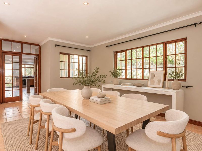 A bright and well-maintained dining room featuring tiled flooring, timber-framed windows, and elegant glass-panelled doors leading to an adjacent space.