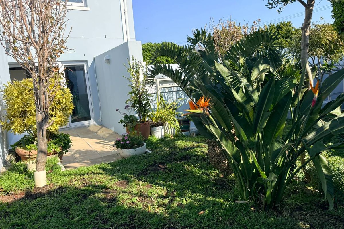 A private rear garden area featuring a paved patio, established landscaping, and direct access to the home via a glass sliding door.