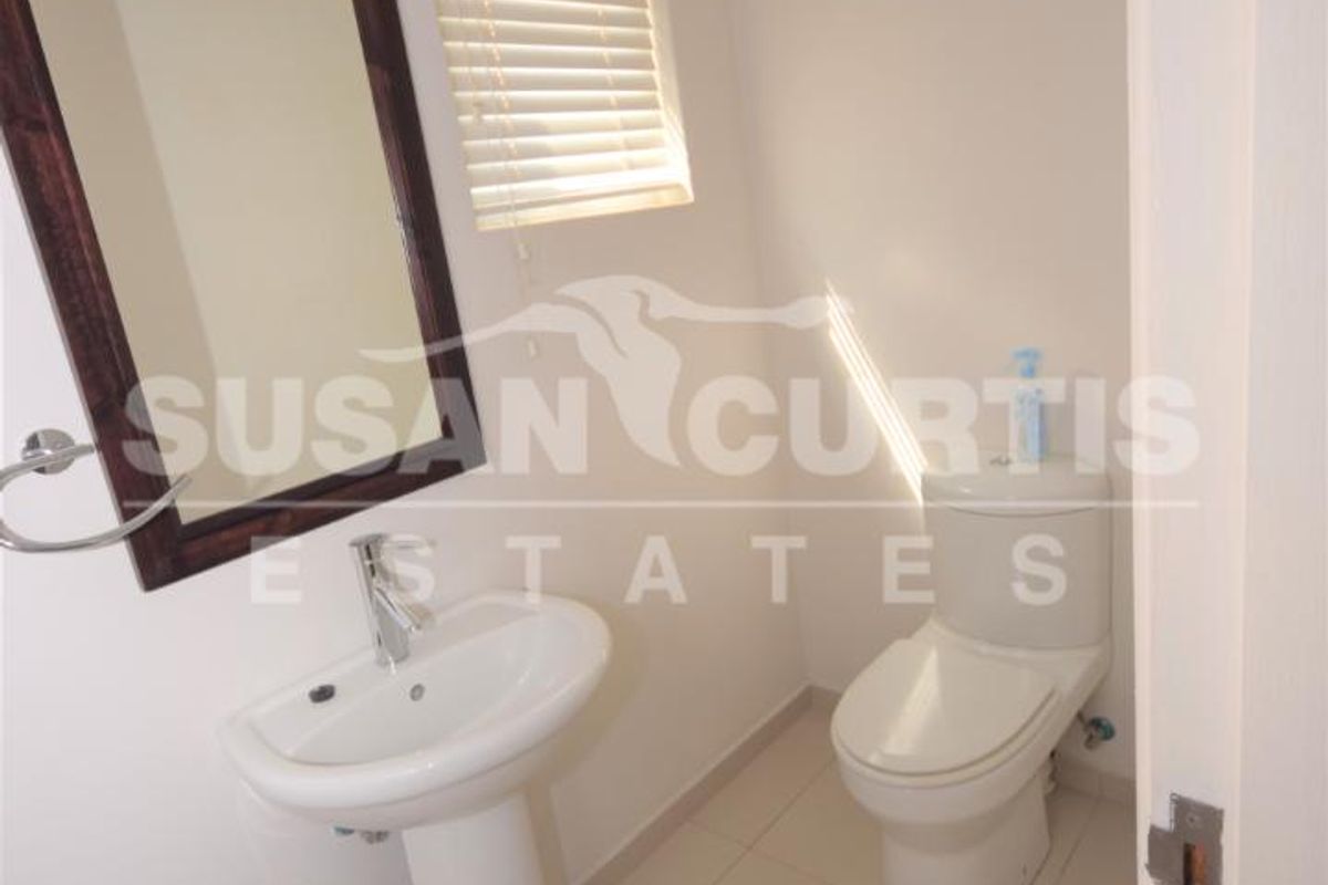 A compact guest bathroom featuring a pedestal sink, modern toilet, and tiled flooring.
