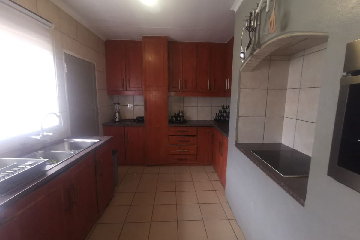 A functional kitchen featuring wooden cabinetry, a double basin sink, built-in oven, and electric hob with tiled flooring and backsplash.