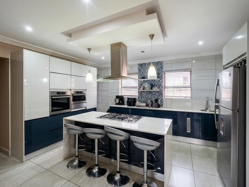 Modern kitchen featuring high-gloss cabinetry, a central island with a gas cooktop, stone countertops, and integrated appliances with stylish mosaic tile accents.