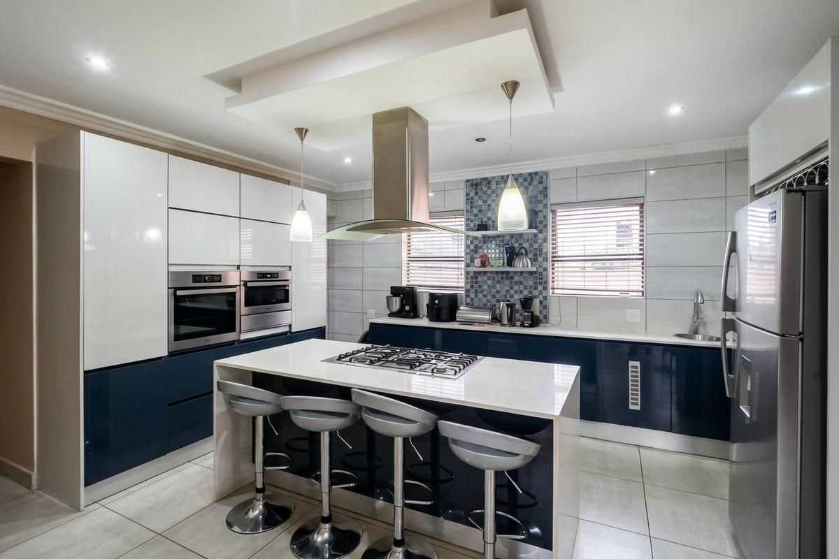 Modern kitchen featuring high-gloss cabinetry, a central island with a gas cooktop, stone countertops, and integrated appliances with stylish mosaic tile accents.
