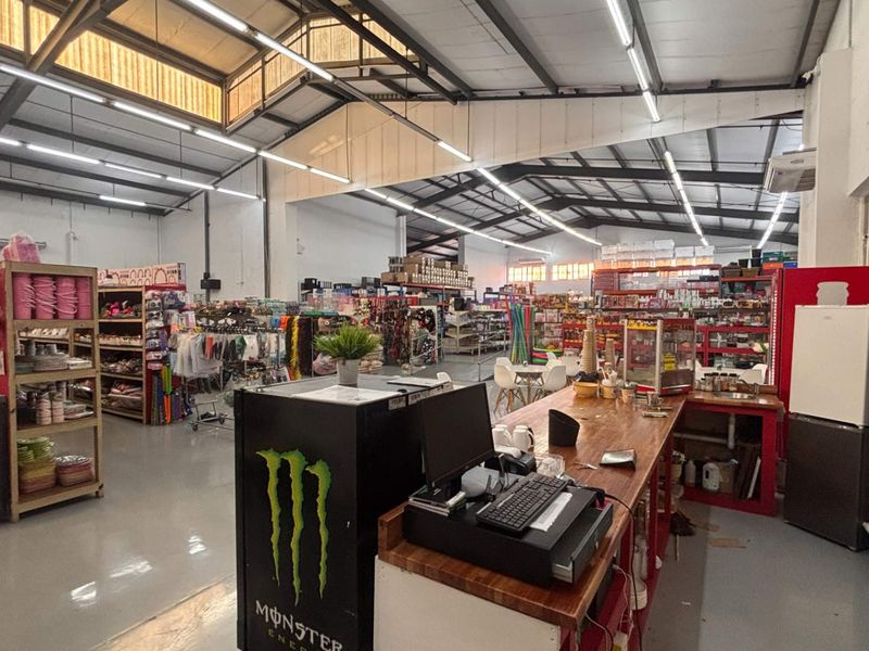 Spacious retail open-plan area featuring high ceilings with exposed steel trusses, polished concrete floors, and integrated service counter with overhead lighting.