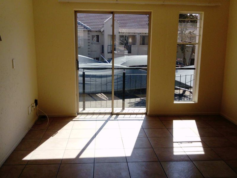 An empty living room featuring tiled flooring, a sliding glass door leading to a balcony, and natural light through a vertical window.