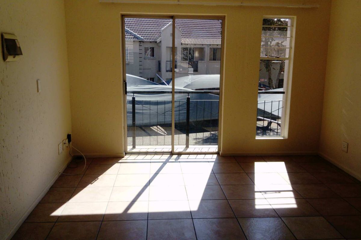 An empty living room featuring tiled flooring, a sliding glass door leading to a balcony, and natural light through a vertical window.
