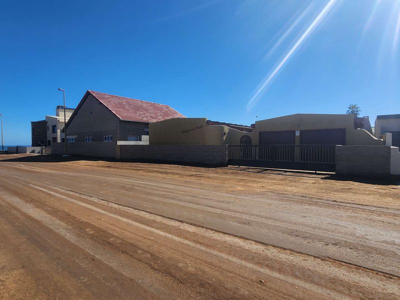 Street view of the property exterior showing the perimeter wall, gated entrance, and garage access with a coastal backdrop.