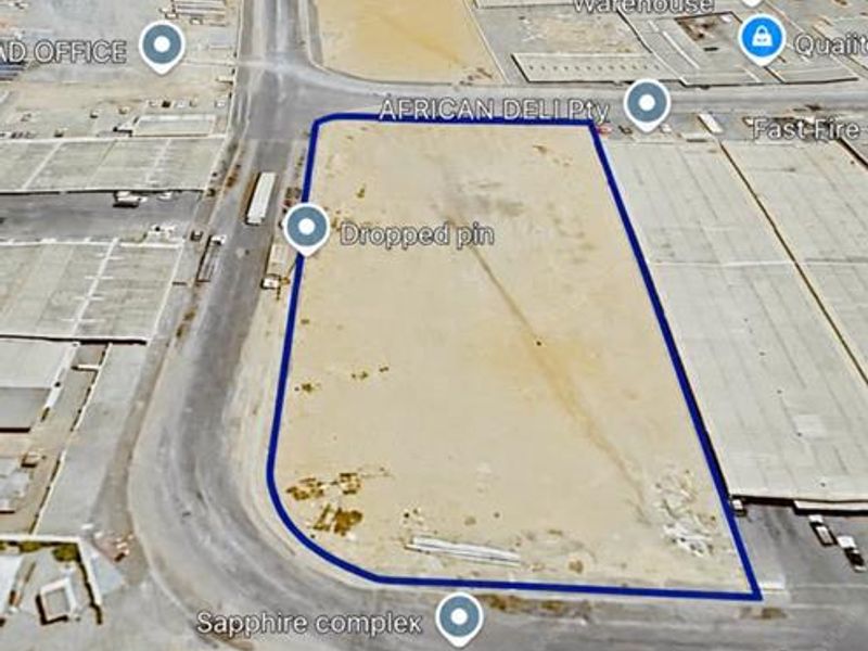 An aerial view of a vacant industrial plot located within a commercial complex, featuring clear road access and surrounding industrial infrastructure.