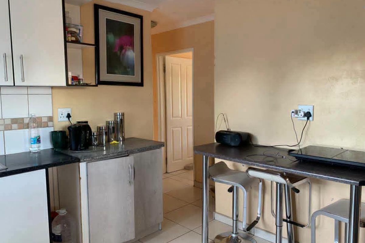 Compact kitchen area featuring built-in cabinetry, tiled backsplash, and a breakfast bar, leading into a hallway.