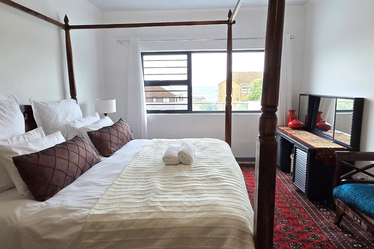 A bedroom featuring a four-poster bed frame and a window with horizontal security bars, offering a functional and comfortable living space.