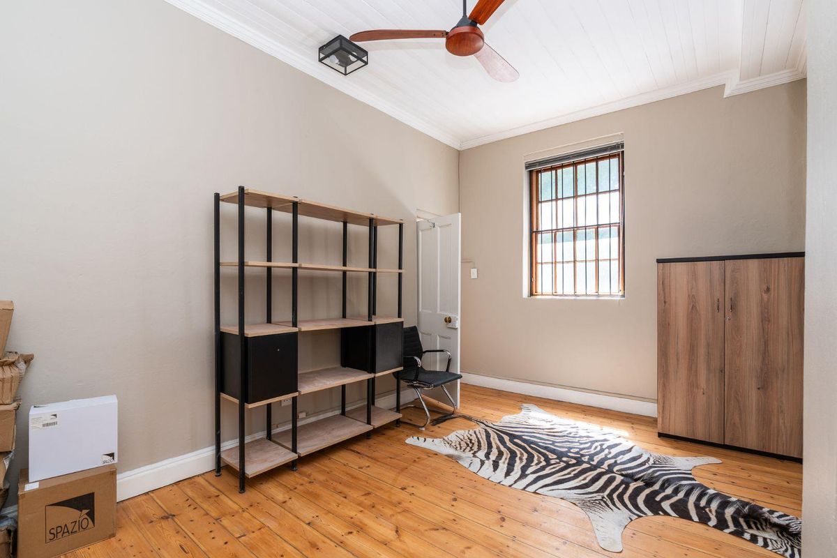 A bedroom featuring polished timber flooring, a ceiling fan, and a window fitted with security bars.