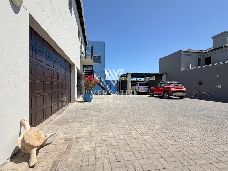 Spacious paved driveway area featuring a double garage, covered carport, and external staircase access to the upper level of the property.