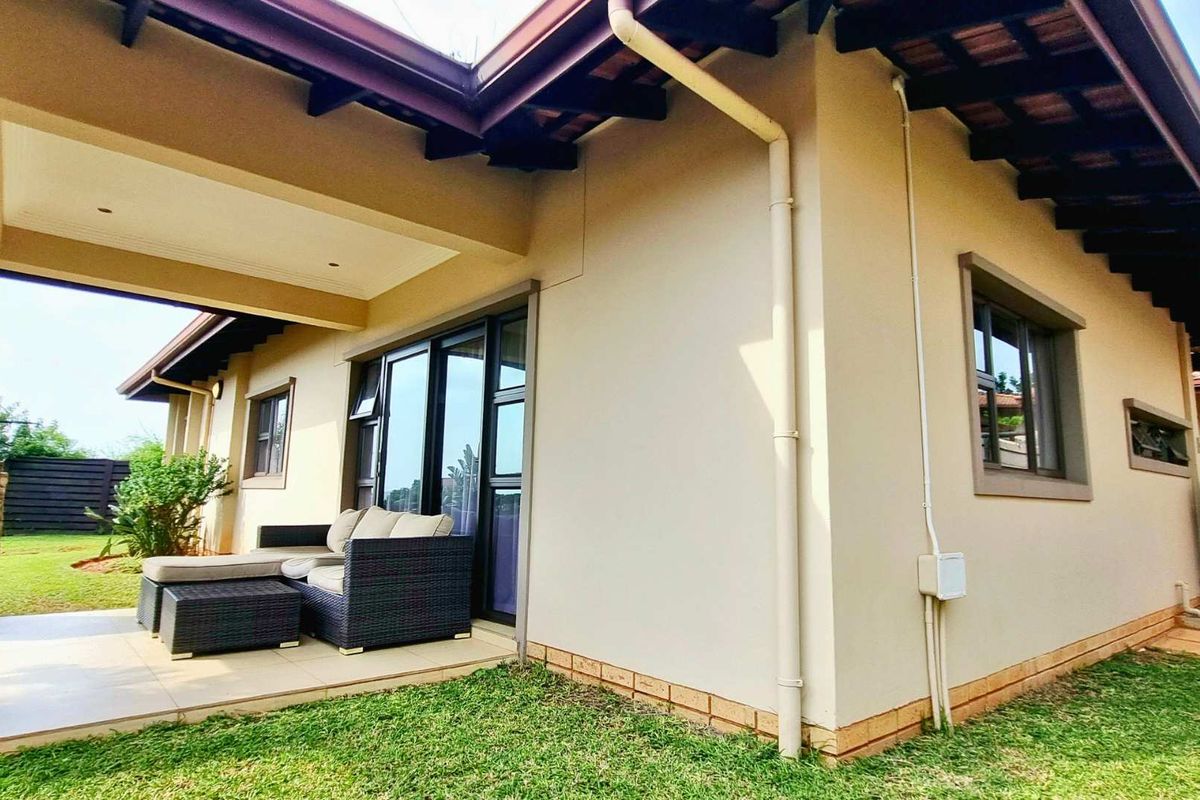 Rear view of the townhouse featuring a covered patio with stone pillar detail, tiled flooring, and access via sliding glass doors to the garden.