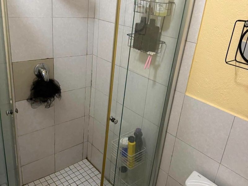 A compact bathroom featuring a glass-enclosed shower with a rainfall shower head and a standard toilet, requiring some cosmetic updates to the finishes.