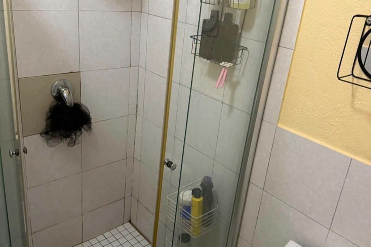 A compact bathroom featuring a glass-enclosed shower with a rainfall shower head and a standard toilet, requiring some cosmetic updates to the finishes.