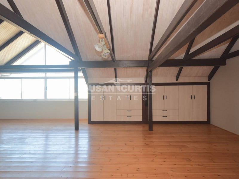Spacious attic-style bedroom featuring vaulted timber ceilings, exposed beams, polished timber flooring, and extensive built-in storage cabinetry.