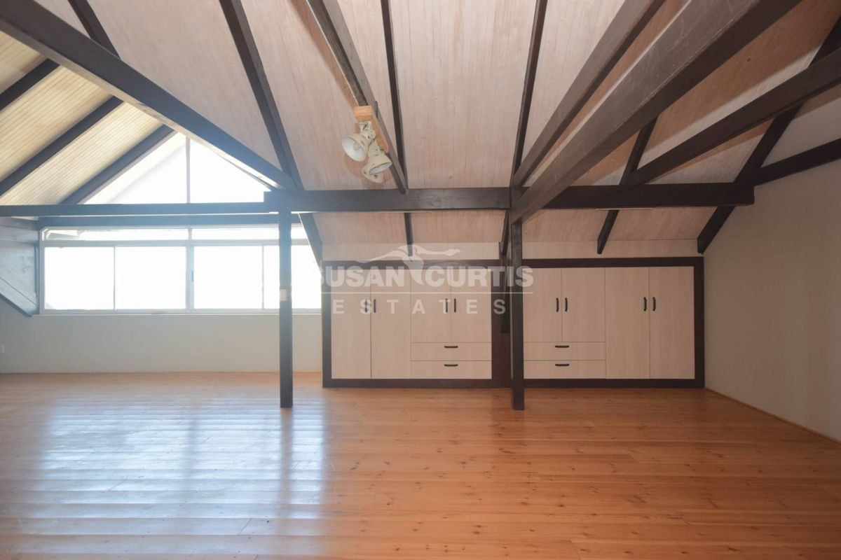 Spacious attic-style bedroom featuring vaulted timber ceilings, exposed beams, polished timber flooring, and extensive built-in storage cabinetry.