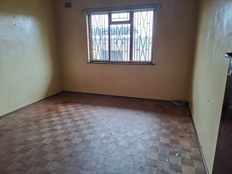 An empty bedroom featuring original parquet flooring, security bars on the window, and walls in need of cosmetic attention.