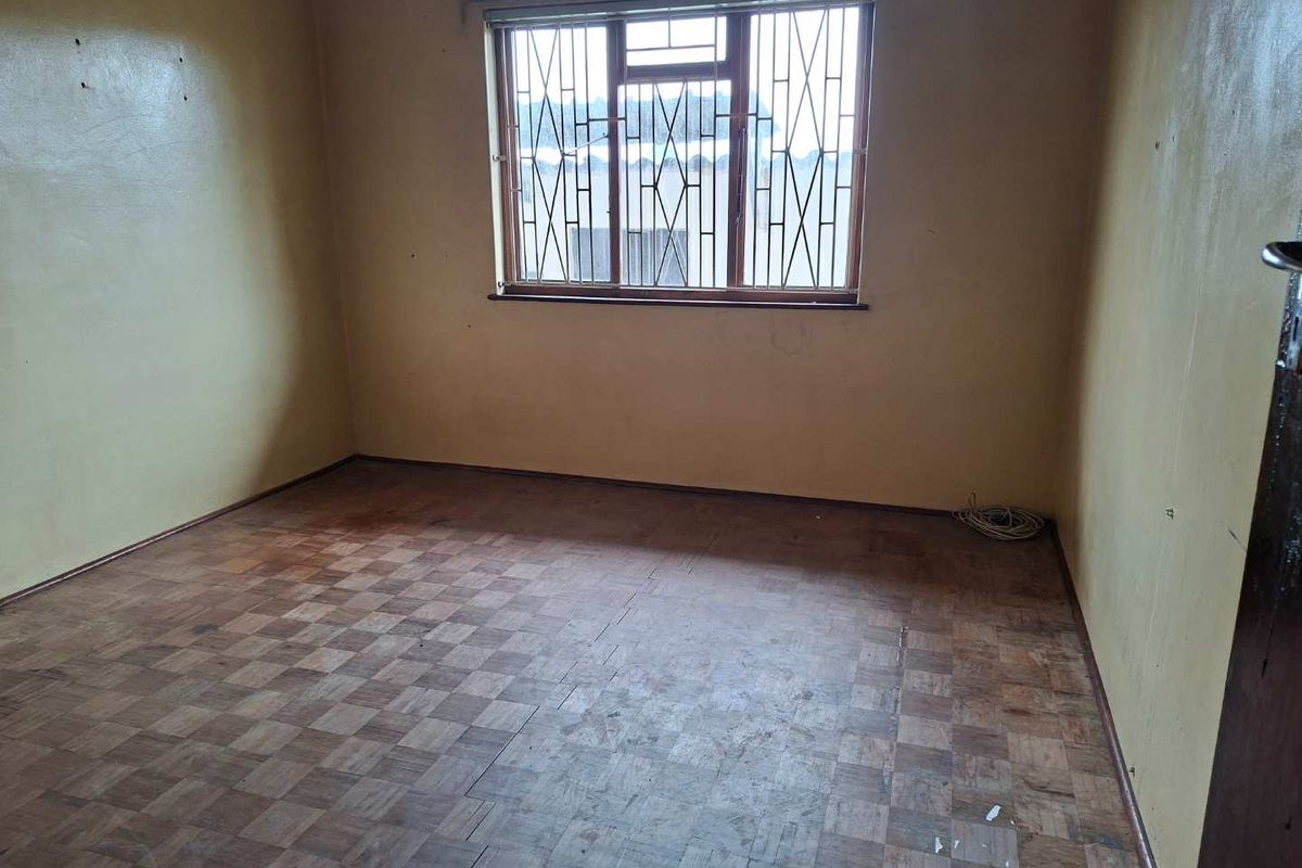 An empty bedroom featuring original parquet flooring, security bars on the window, and walls in need of cosmetic attention.