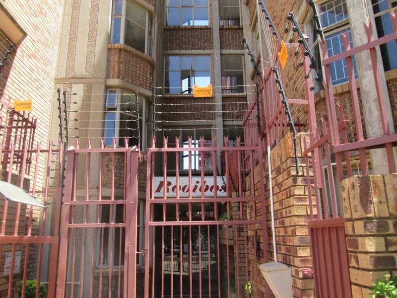 Front entrance view of the apartment building featuring a brick facade, secure metal gate, and perimeter electric fencing.