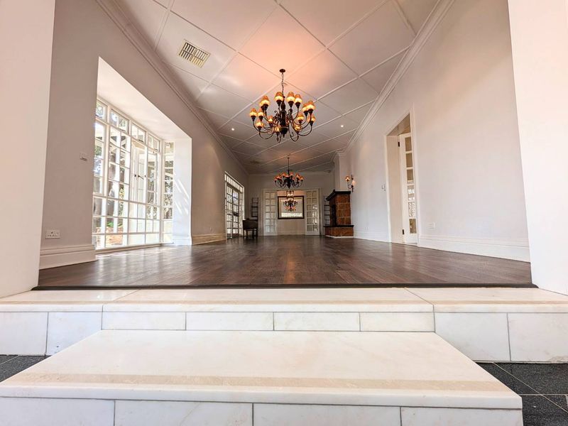 Spacious living area featuring dark hardwood flooring, a coffered ceiling, stone fireplace, and elegant chandeliers, accessed via marble steps.