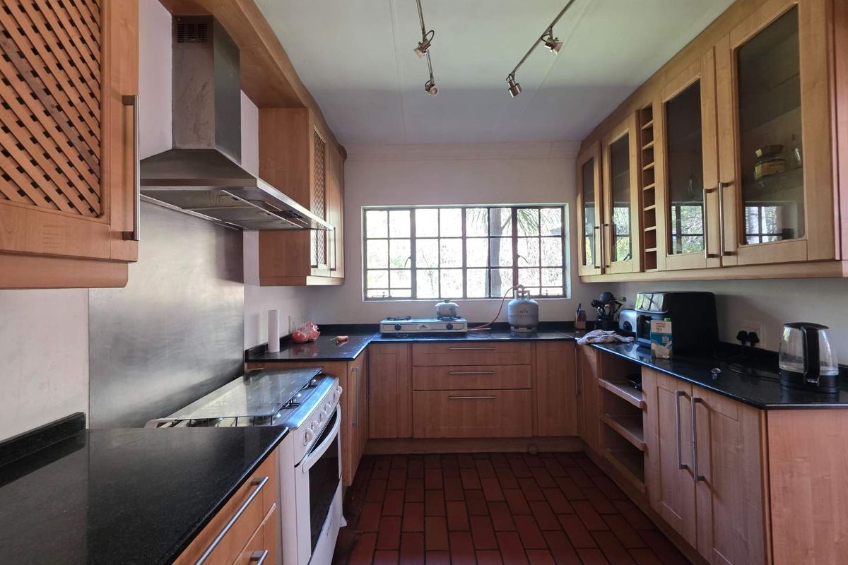 A functional kitchen featuring wooden cabinetry, black granite countertops, a stainless steel extractor fan, and a classic brick-tiled floor.