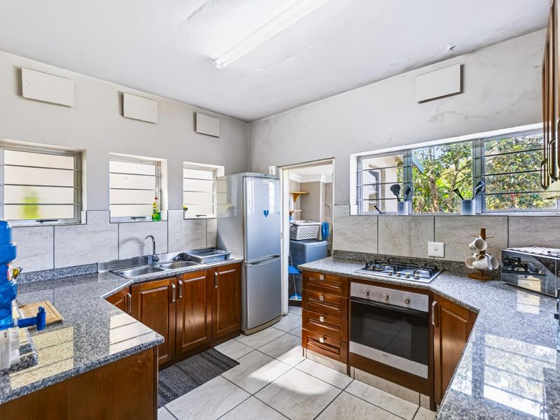 Functional kitchen featuring granite countertops, wooden cabinetry, built-in oven, gas hob, and tiled finishes, with an adjacent scullery area.