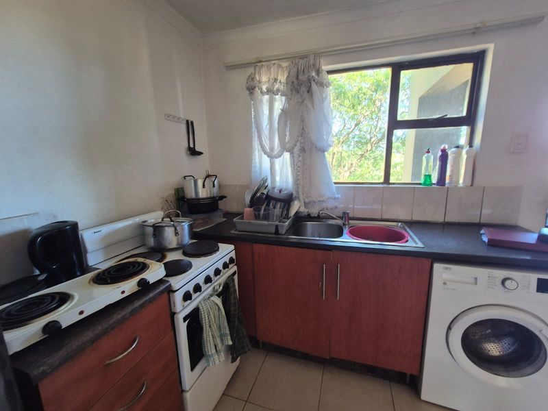 A compact kitchen featuring built-in cabinetry, laminate countertops, a stainless steel sink, and a freestanding stove with tiled splashback and flooring.