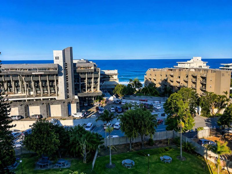 Elevated view overlooking the surrounding apartment complex, parking area, landscaped gardens, and the ocean horizon.