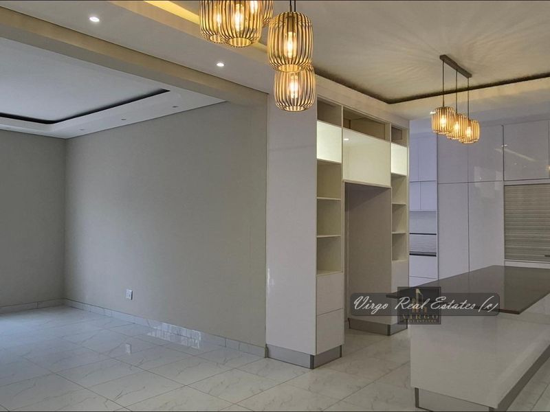 Modern open-plan living and kitchen area featuring high-gloss cabinetry, a central island, recessed lighting, and polished tiled flooring throughout.