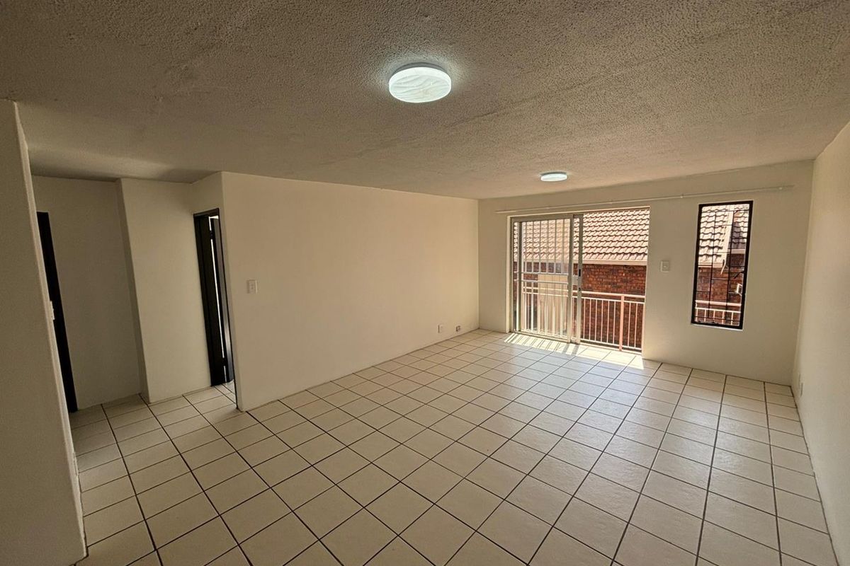 An empty, open-plan living area featuring tiled flooring, textured ceilings, and a sliding glass door leading to a balcony.