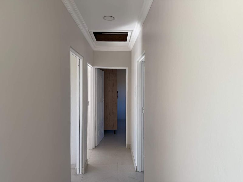 A neutral-toned hallway featuring tiled flooring, ceiling cornicing, and a loft access hatch, providing access to multiple rooms within the townhouse.
