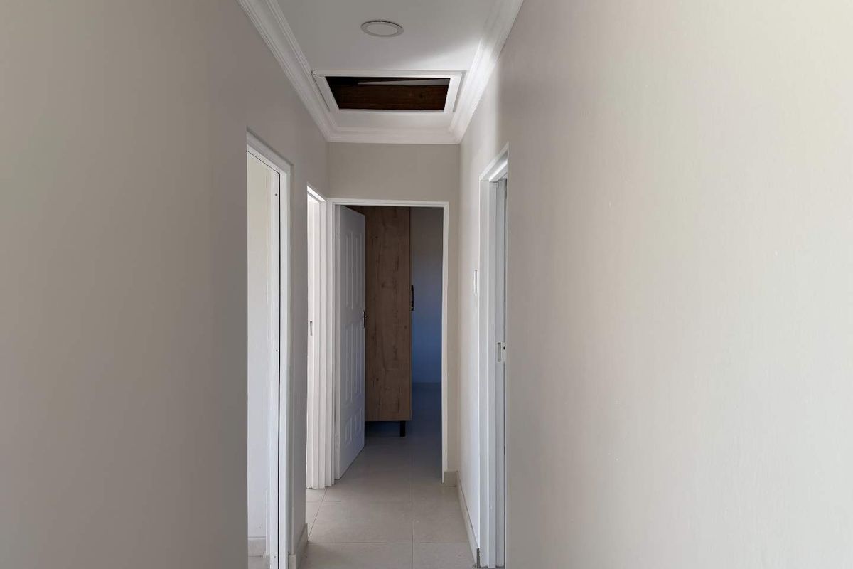 A neutral-toned hallway featuring tiled flooring, ceiling cornicing, and a loft access hatch, providing access to multiple rooms within the townhouse.