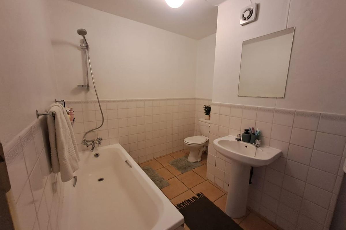 A functional bathroom featuring a bathtub with shower mixer, pedestal basin, and toilet, finished with classic white wall tiling and ceramic floor tiles.