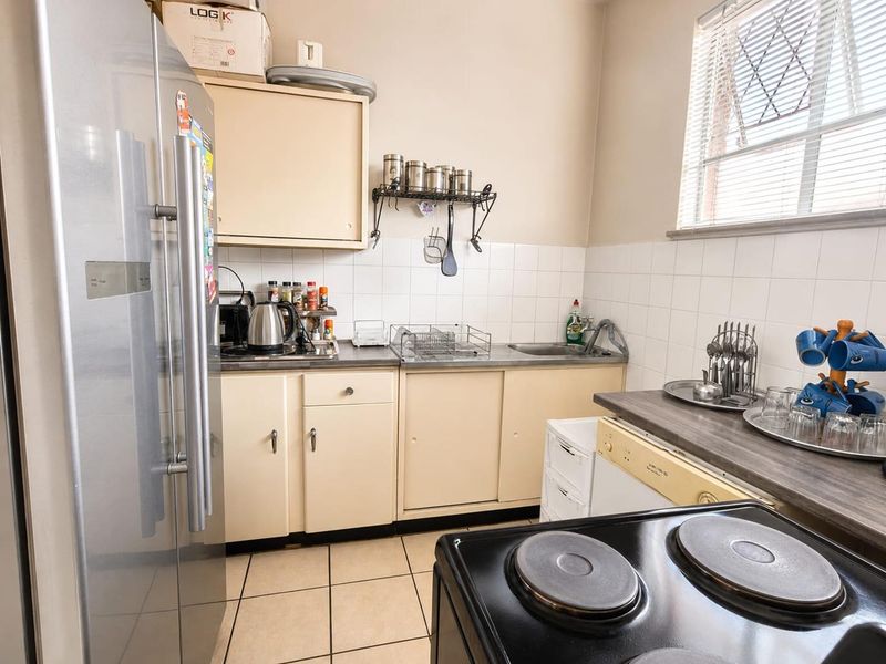 A functional kitchen featuring built-in cabinetry, a stainless steel sink, tiled backsplash, and tiled flooring, offering a practical layout for daily meal preparation.