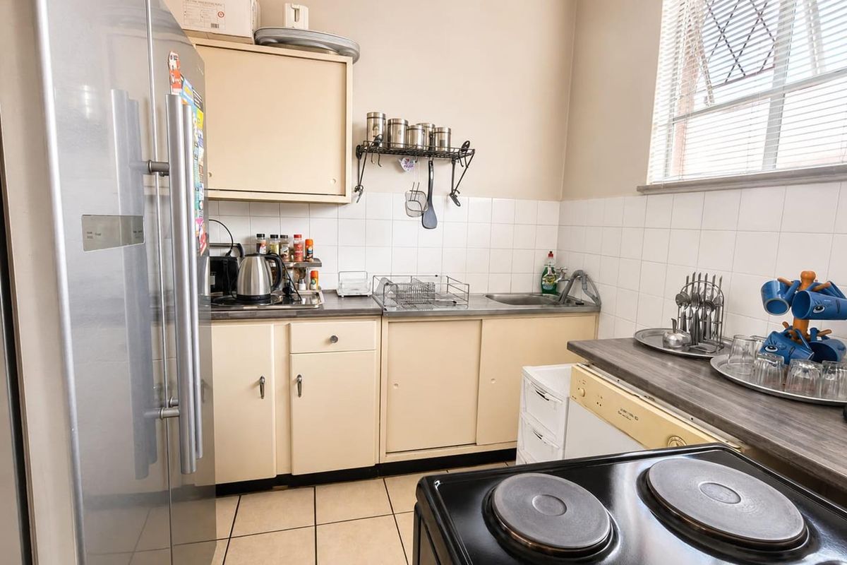 A functional kitchen featuring built-in cabinetry, a stainless steel sink, tiled backsplash, and tiled flooring, offering a practical layout for daily meal preparation.
