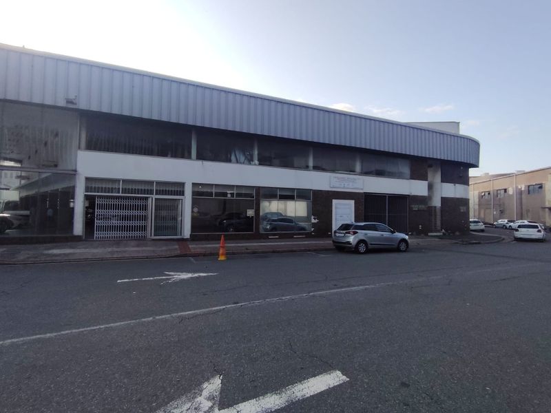 Street-level view of a commercial retail property featuring large display windows, metal cladding, and secure access points along the main road.