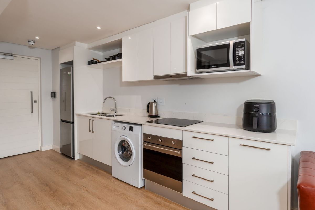 Modern kitchen featuring sleek white cabinetry, stone countertops, integrated appliances including an oven, hob, and washing machine, with recessed lighting.
