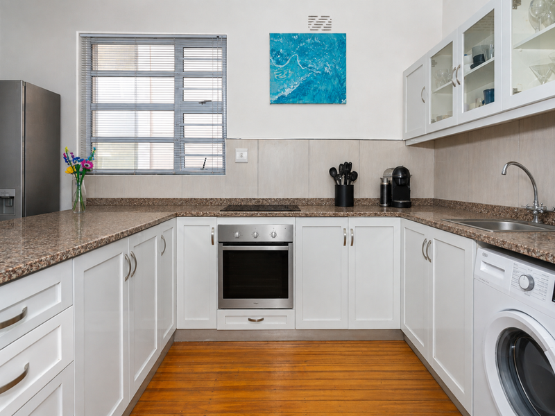 A well-maintained kitchen featuring white shaker-style cabinetry, granite countertops, built-in oven, electric hob, and integrated laundry facilities with warm timber flooring.