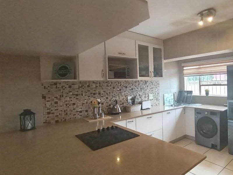 A functional kitchen featuring stone countertops, a mosaic tile backsplash, built-in cabinetry, and an integrated electric hob with ample workspace.