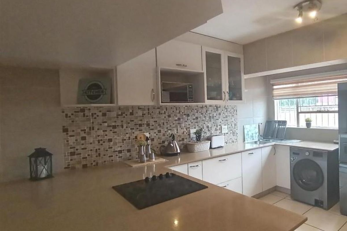 A functional kitchen featuring stone countertops, a mosaic tile backsplash, built-in cabinetry, and an integrated electric hob with ample workspace.