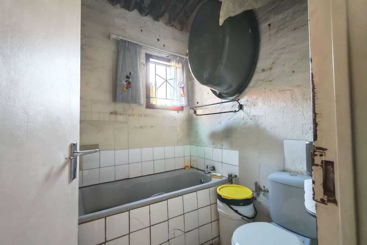 A small bathroom featuring a bathtub and toilet, requiring significant renovation and cosmetic updates to improve the overall condition and finish.