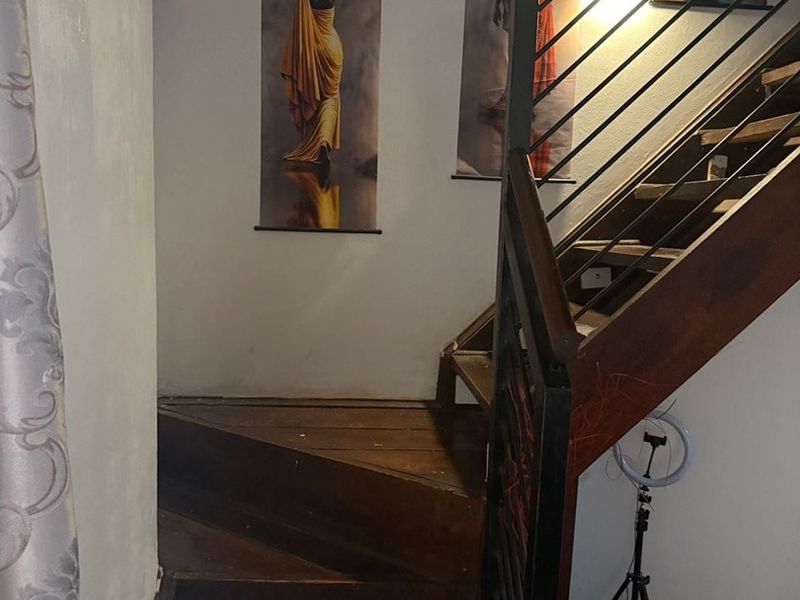 A hallway featuring a wooden staircase with a metal balustrade and tiled flooring, providing access to the upper level of the apartment.
