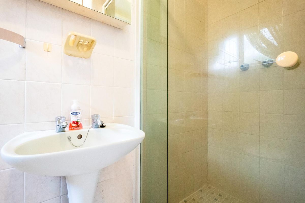 A functional bathroom featuring a pedestal sink, wall-mounted mirror cabinet, and a glass-enclosed shower stall with tiled walls.